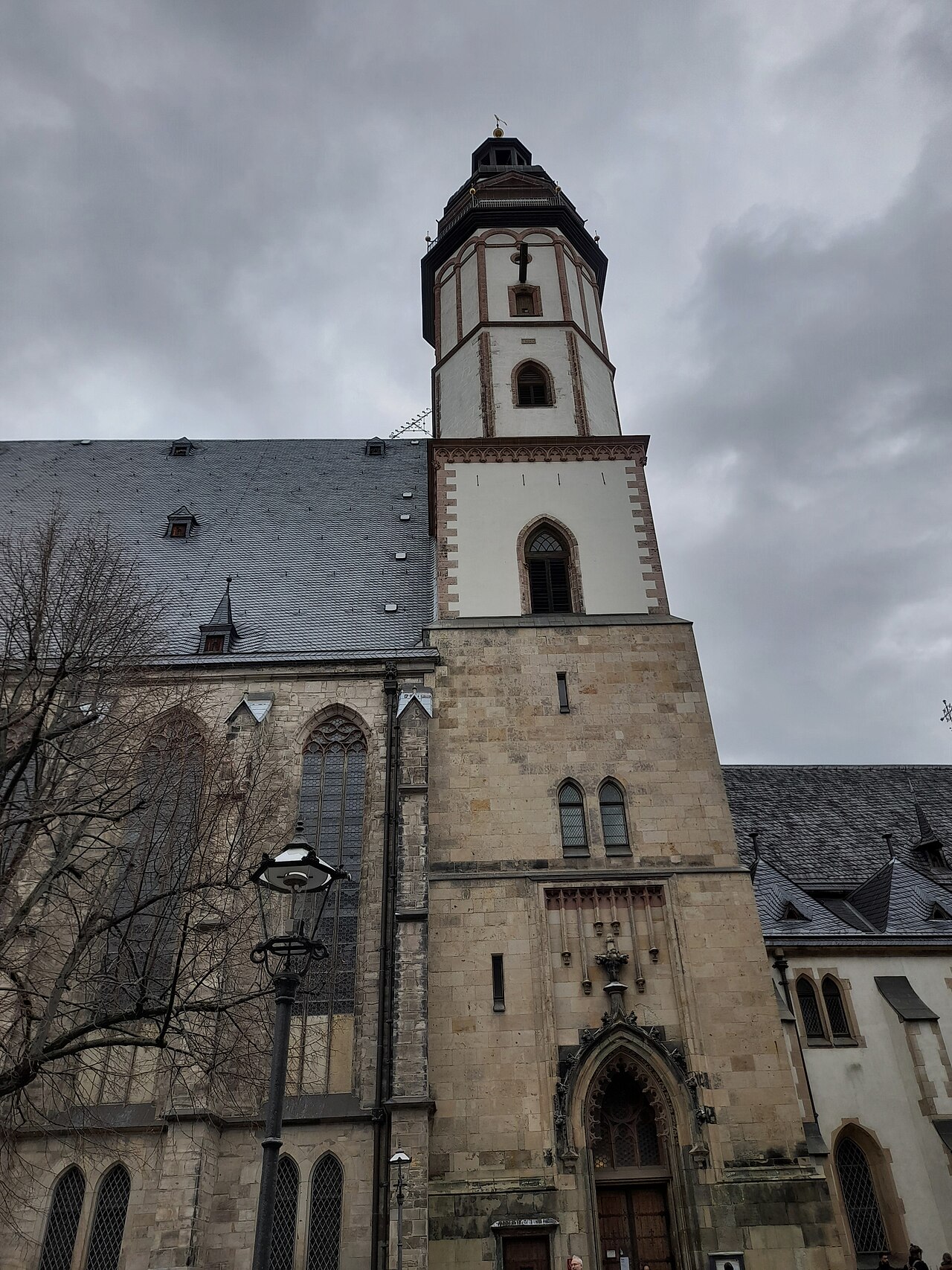 Exterior da Thomaskirche, com janelas ogivais, telhado escuro e torre alta, sob céu encoberto.