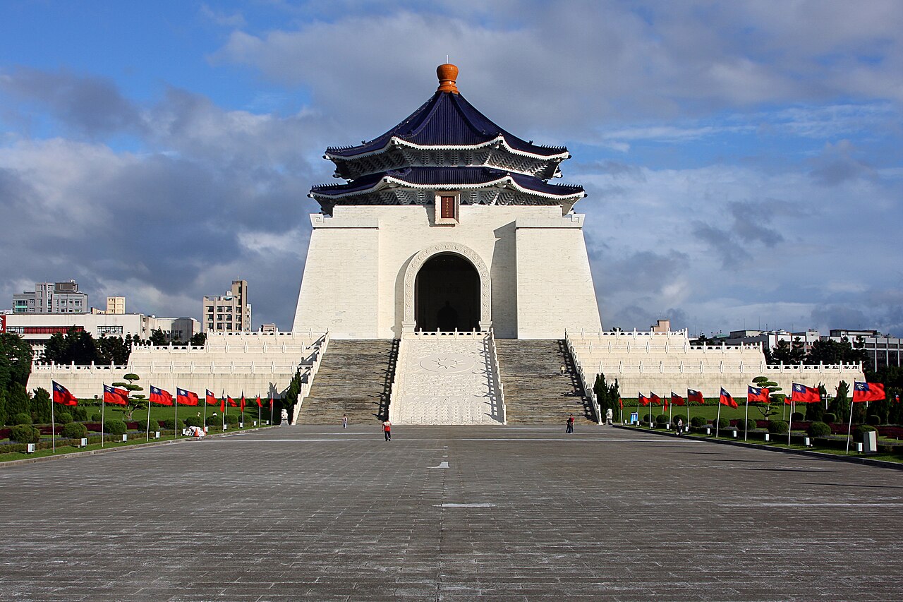 Memorial Chiang Kai-shek com fachada branca, telhado azul, grande escadaria e praça com jardins e bandeiras.