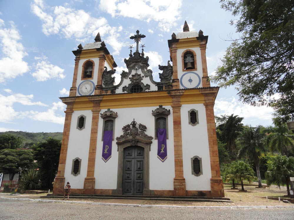 Fachada da Igreja do Carmo com paredes brancas, detalhes amarelos e alaranjados, duas torres e entrada de cantaria trabalhada.