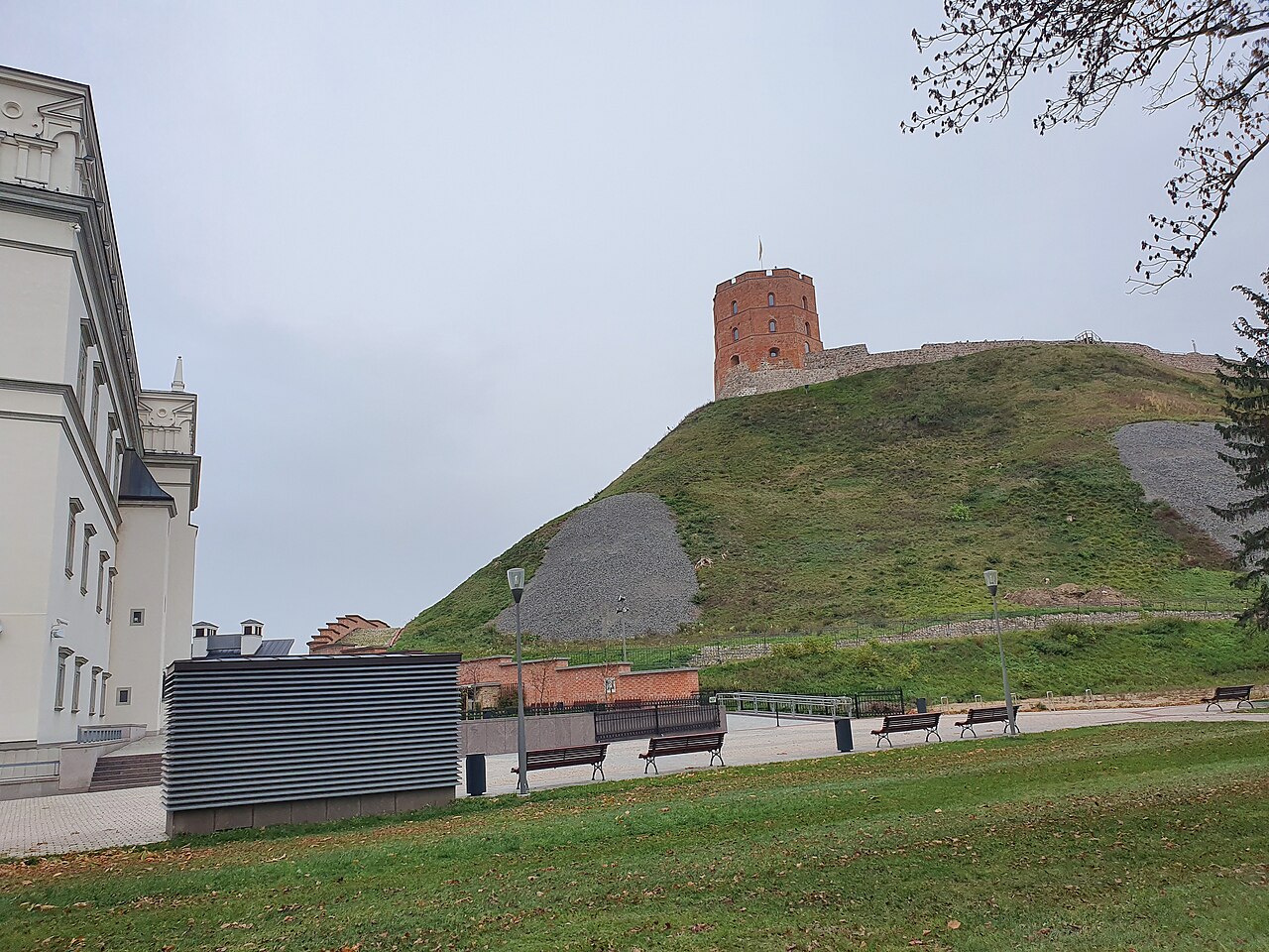 Torre de tijolos vermelhos no alto de uma colina gramada, junto a muralhas de pedra, sob céu encoberto.