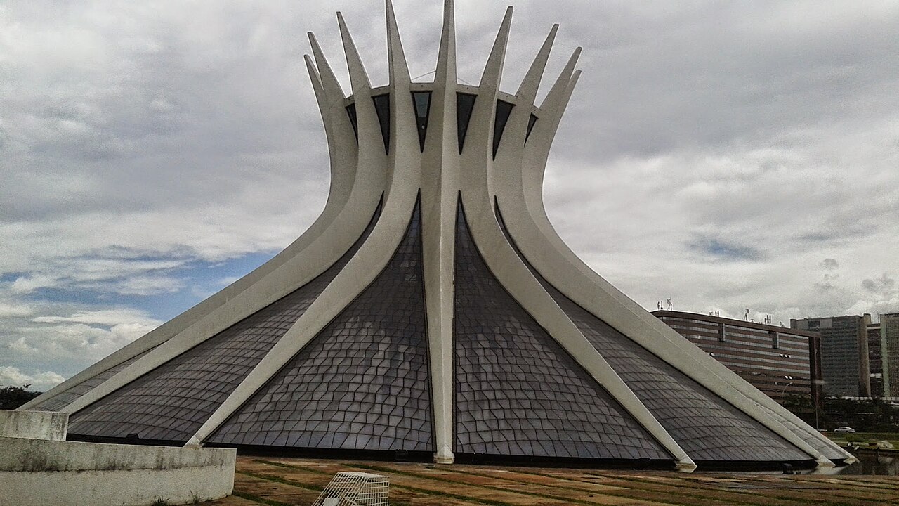 Vista externa da Catedral de Brasília, com pilares brancos curvos, superfícies envidraçadas escuras e gramado em primeiro plano.