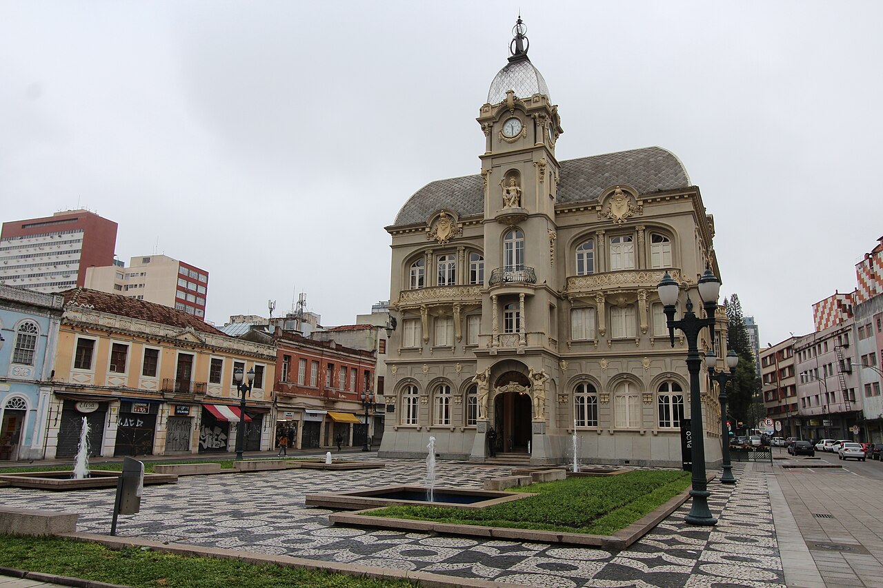 Fachada ornamentada do Paço da Liberdade, com torre, relógio e cúpula, diante de praça com fontes e canteiros.