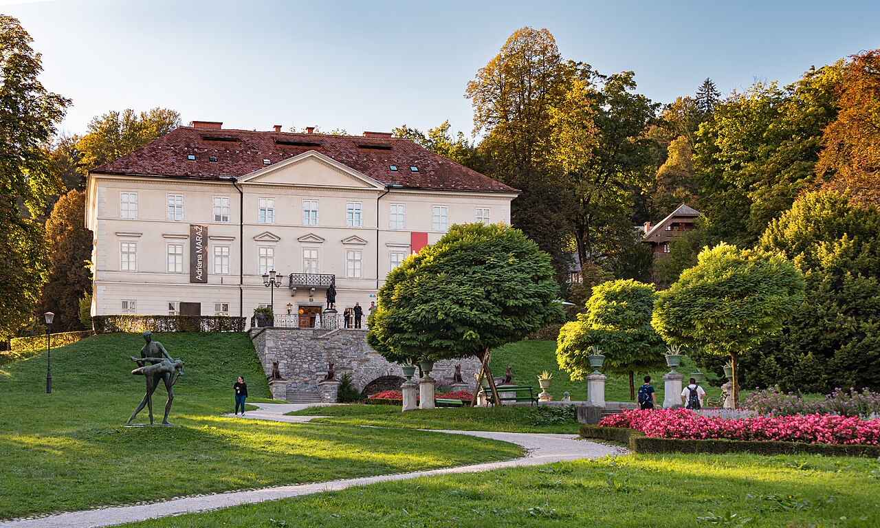 Fachada clara do Palácio Tivoli com telhado avermelhado, escadarias de pedra, esculturas, jardins e visitantes à frente.