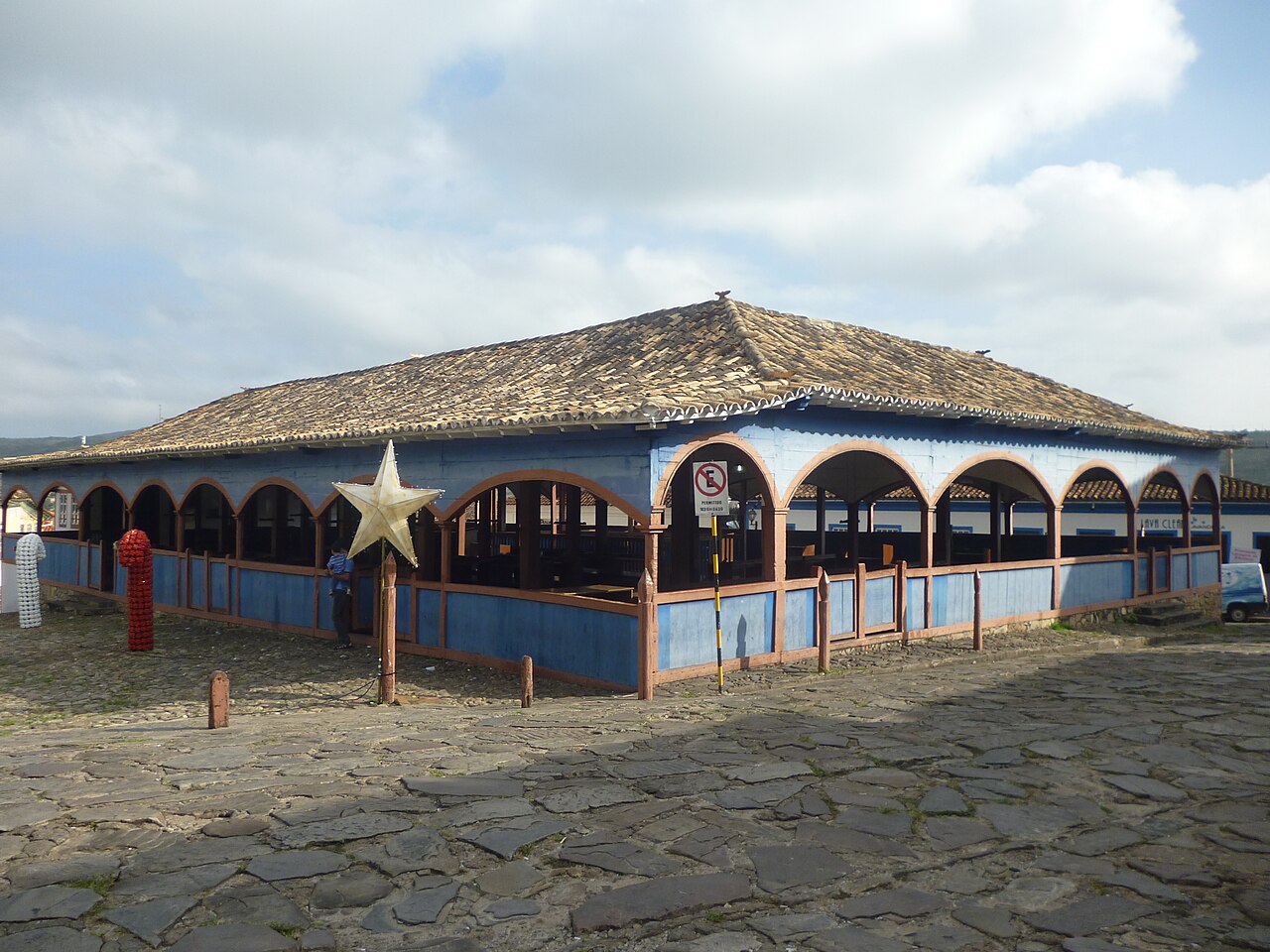 Edifício do Mercado Velho com paredes azuis, arcadas em tom salmão e telhado cerâmico diante de rua de pedras.