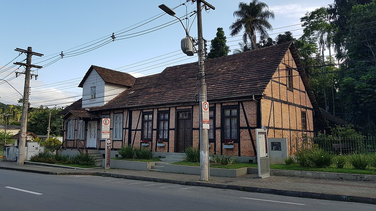 Fachada do Museu da Família Colonial com tijolos aparentes, estrutura escura em enxaimel, telhado inclinado e floreiras.