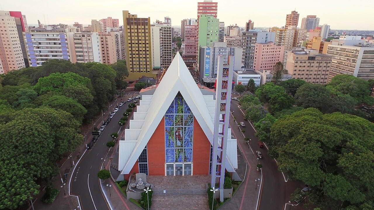 Vista elevada da Catedral de Londrina, com cobertura branca triangular, fachada avermelhada, vitral vertical e torre estreita.