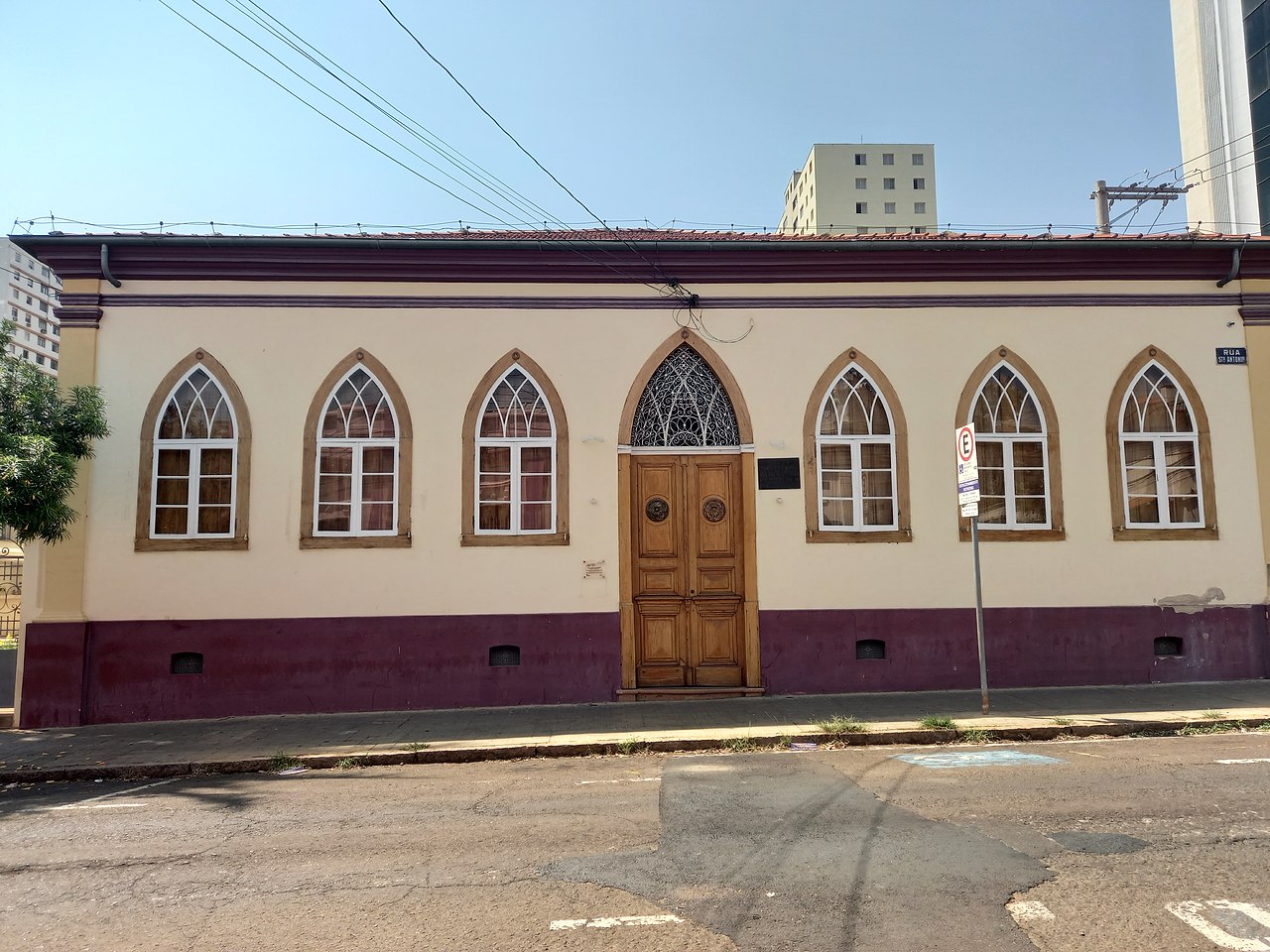 Fachada térrea creme com base vinho, seis janelas de arcos ogivais e porta central de madeira na Casa de Prudente de Moraes.