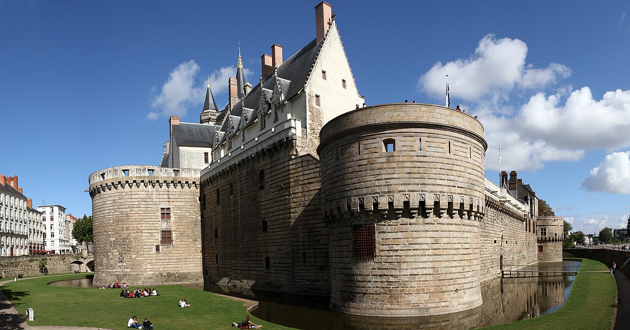 Muralhas de pedra e torres circulares do Château des ducs de Bretagne, com fosso, gramados e edifícios de fachadas claras ao fundo.