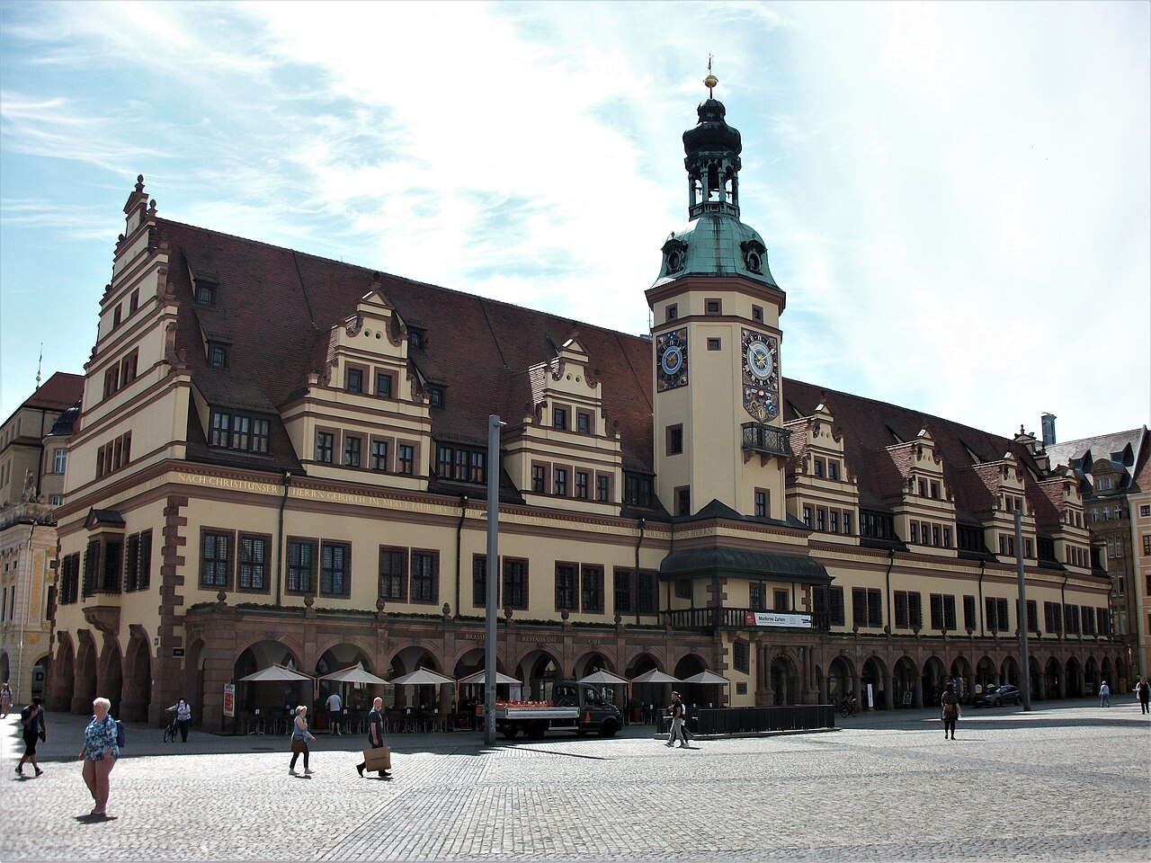 Fachada comprida do Altes Rathaus, com arcadas, telhado inclinado e torre com relógios, diante da praça pavimentada.