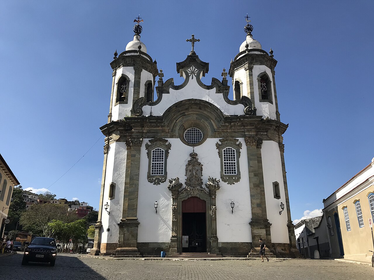 Fachada da Igreja de Nossa Senhora do Carmo, com duas torres, portal ornamentado, calçamento de pedra e pedestres à frente.