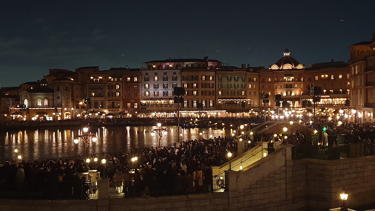 Vista noturna do Mediterranean Harbor, com fachadas iluminadas refletidas na água, no Tokyo DisneySea.