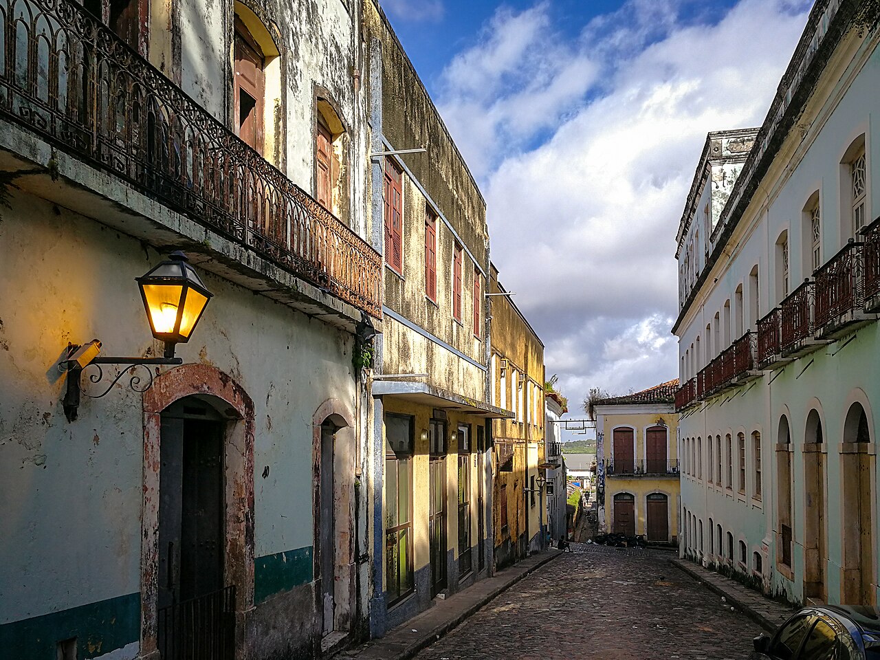 Rua de pedra em declive entre sobrados antigos de fachadas claras, janelas altas e sacadas de ferro no Centro Histórico de São Luís.