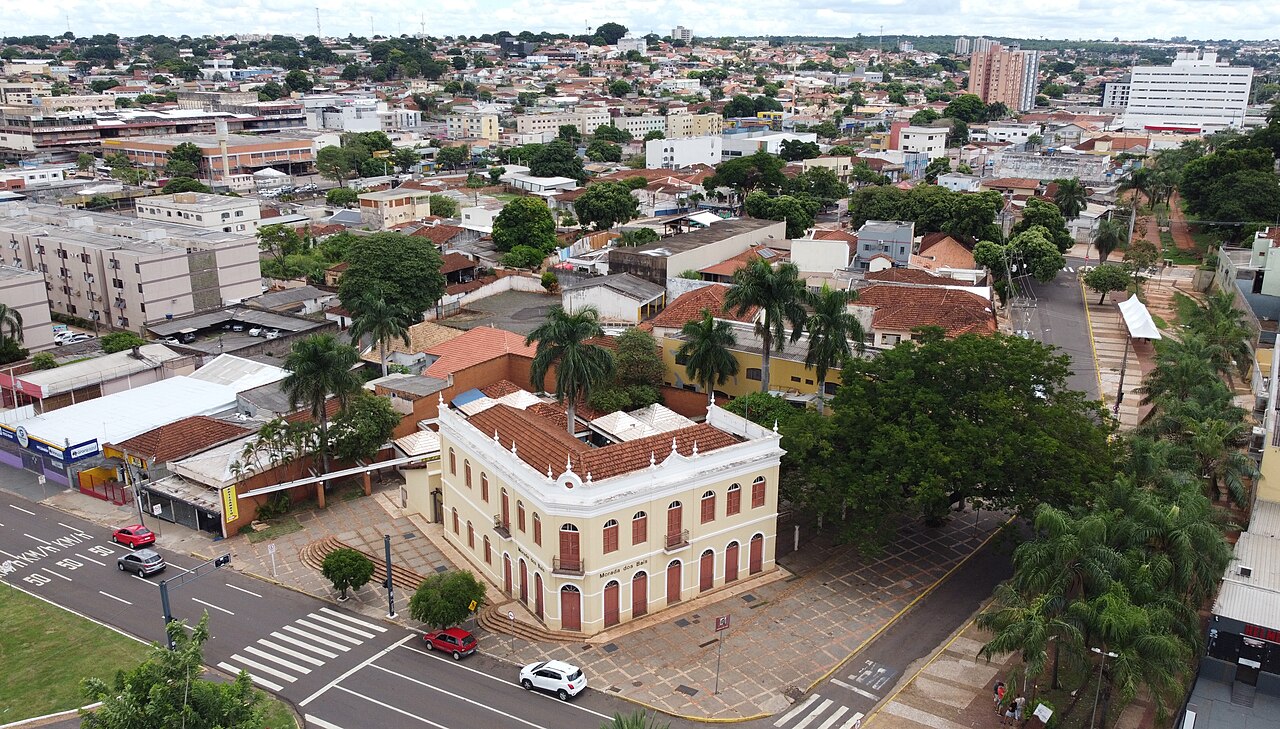 Vista elevada da Morada dos Baís, casarão de dois pavimentos com fachada creme, janelas avermelhadas e telhado cerâmico, cercado por ruas e árvores.