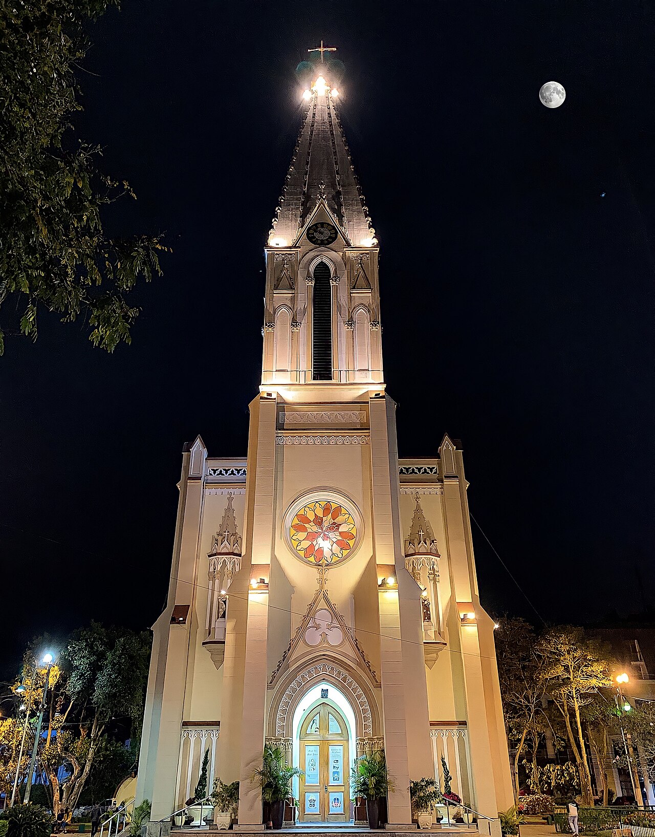 Fachada noturna iluminada da Matriz de Santa Teresa, com torre central, relógio, cruz, rosácea e entrada em arco ogival.