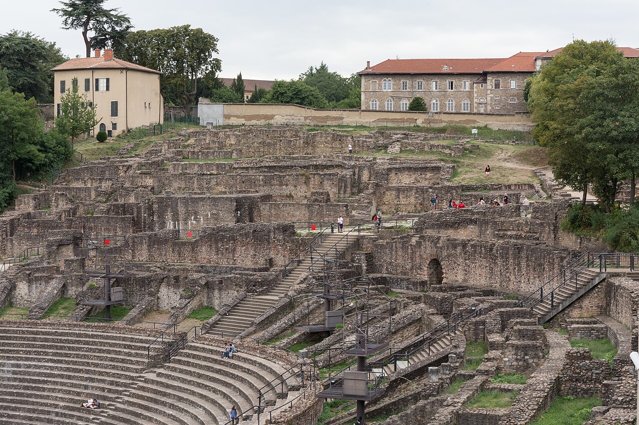 Arquibancadas curvas de pedra do teatro romano de Fourvière, com ruínas, escadarias, passarelas e visitantes dispersos.