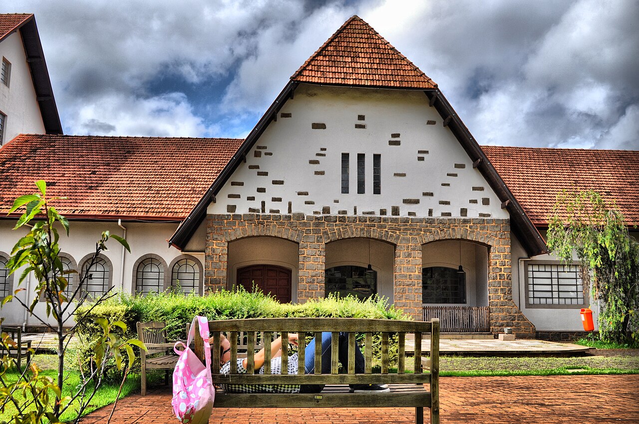 Edifício do Museu Histórico com paredes brancas, telhados vermelhos e entrada de três arcos, diante de jardim e bancos.