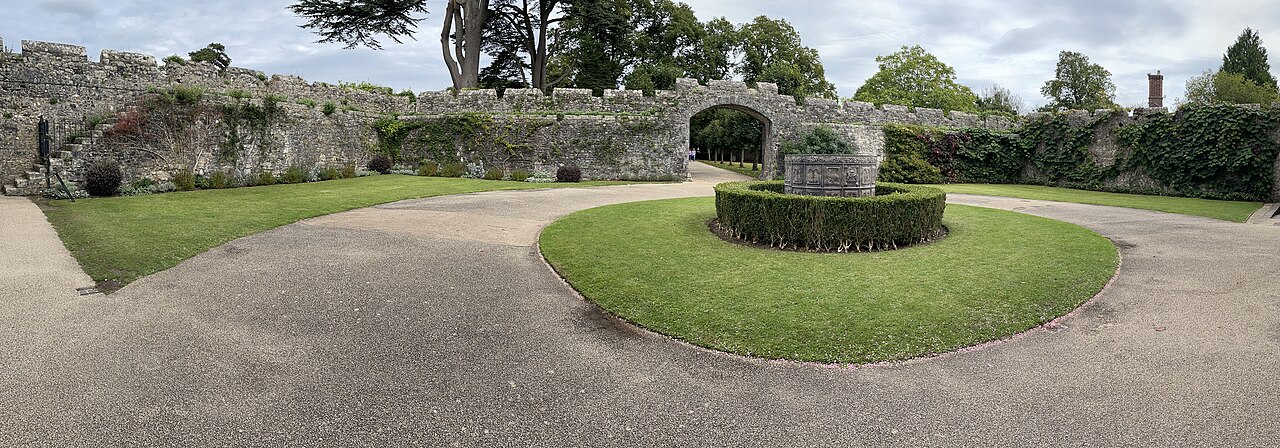Pátio ajardinado de St Fagans Castle, com gramado circular, sebe, estrutura ornamental de pedra e muros com passagem em arco.