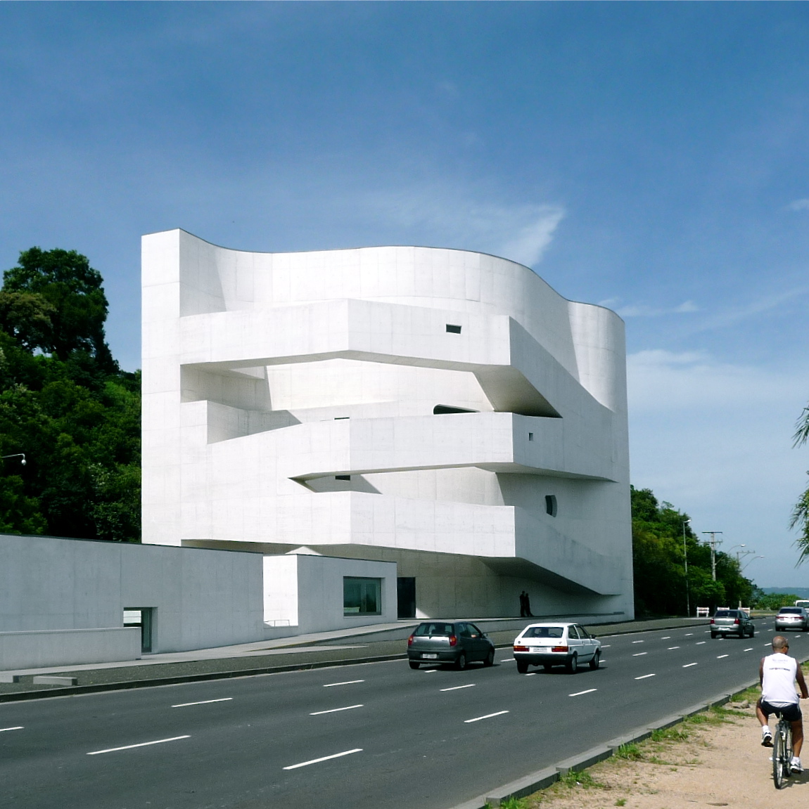 Edifício branco da Fundação Iberê Camargo, com formas curvas e rampas externas em zigue-zague, diante de uma avenida.