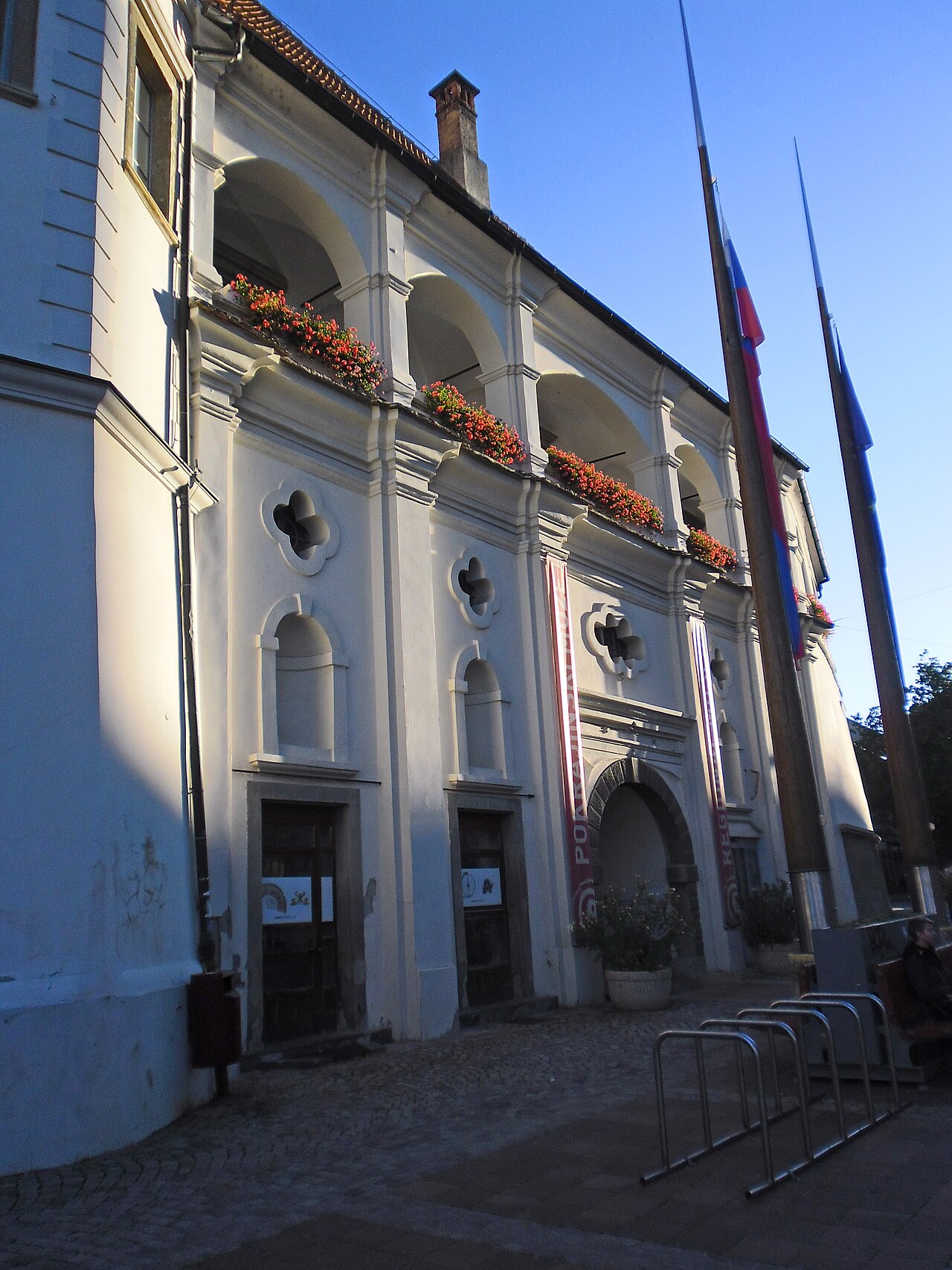 Entrada do Museu Regional no Castelo de Maribor, com portal de pedra escura, galeria superior de arcos e bandeiras.