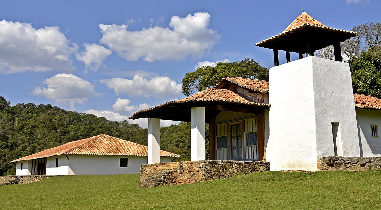 Casa Grande e Capela do Sítio Santo Antônio, com paredes brancas e telhados cerâmicos, sobre gramado cercado por mata.