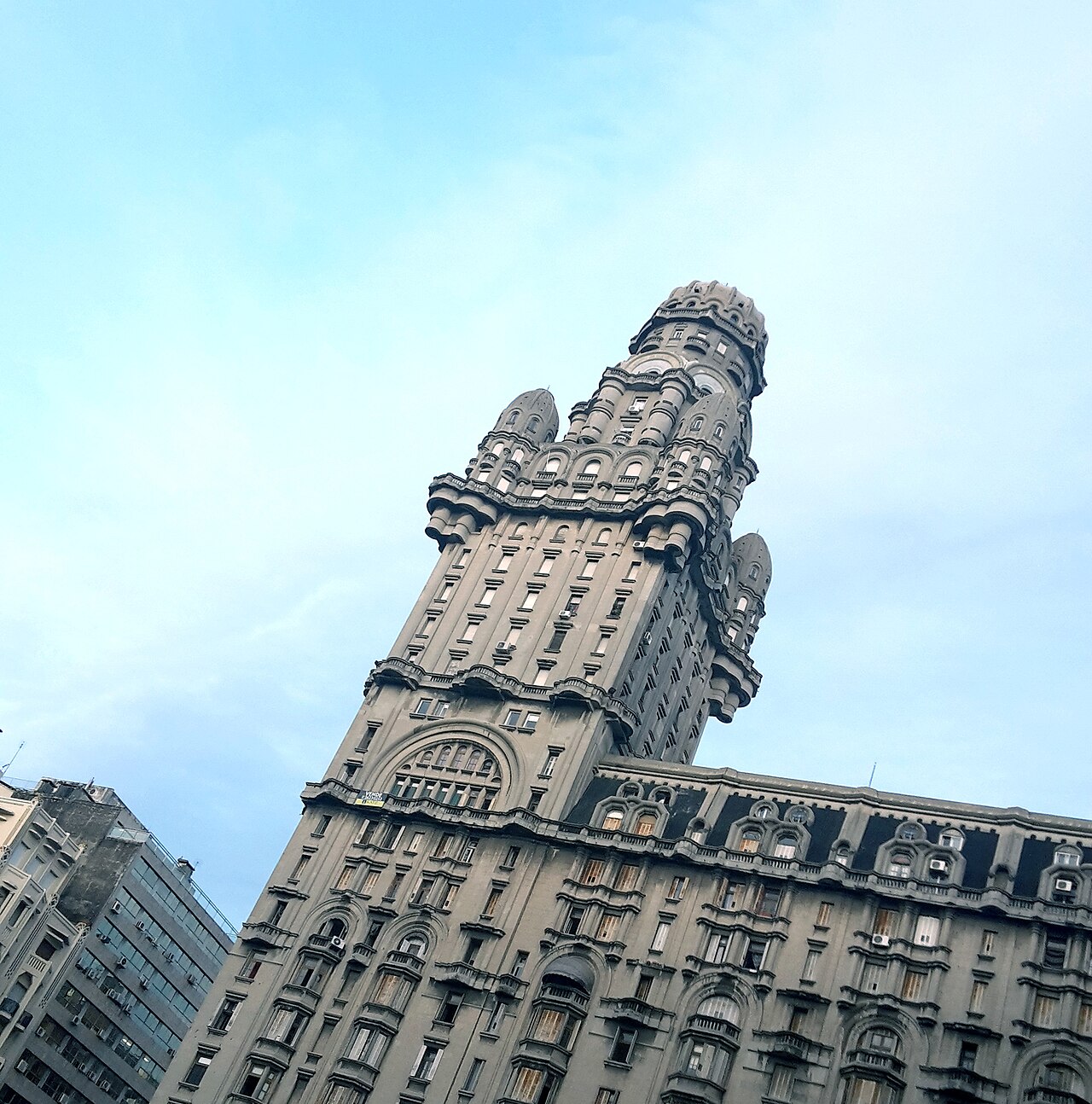 Palacio Salvo visto de baixo em enquadramento inclinado, com fachada ornamentada, torre de volumes arredondados e céu azul-claro.