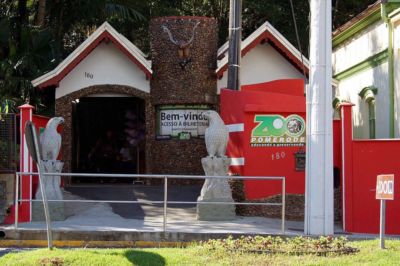 Entrada do Zoo Pomerode com letreiro, muros vermelhos, fachadas brancas e duas esculturas de aves.