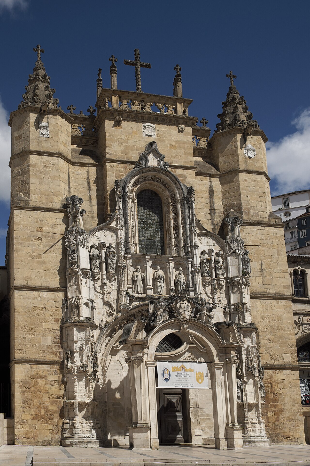 Fachada de pedra clara da Igreja de Santa Cruz, com portal esculpido, estátuas em nichos, janela central e cruzes no coroamento.