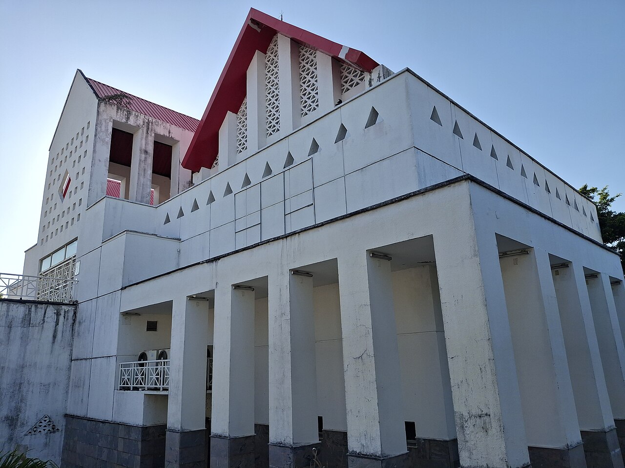Edifício branco do Centro Dragão do Mar visto de baixo, com pilares altos e coberturas vermelhas sob céu azul.