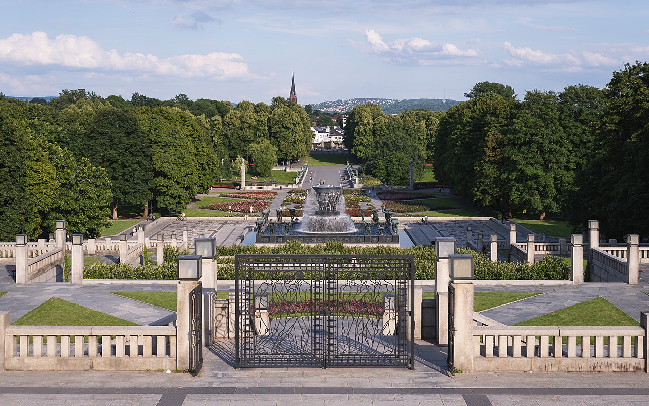 Vista elevada do parque Vigeland com portão de ferro figurativo, terraços de pedra, fonte, esculturas e alameda arborizada.