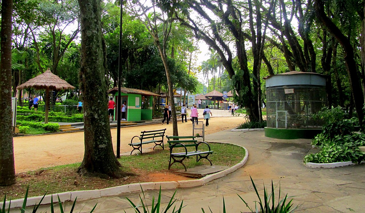 Área arborizada do conjunto do Taquaral, com caminhos, bancos, pessoas caminhando e quiosques com cobertura de palha; a lagoa não aparece.