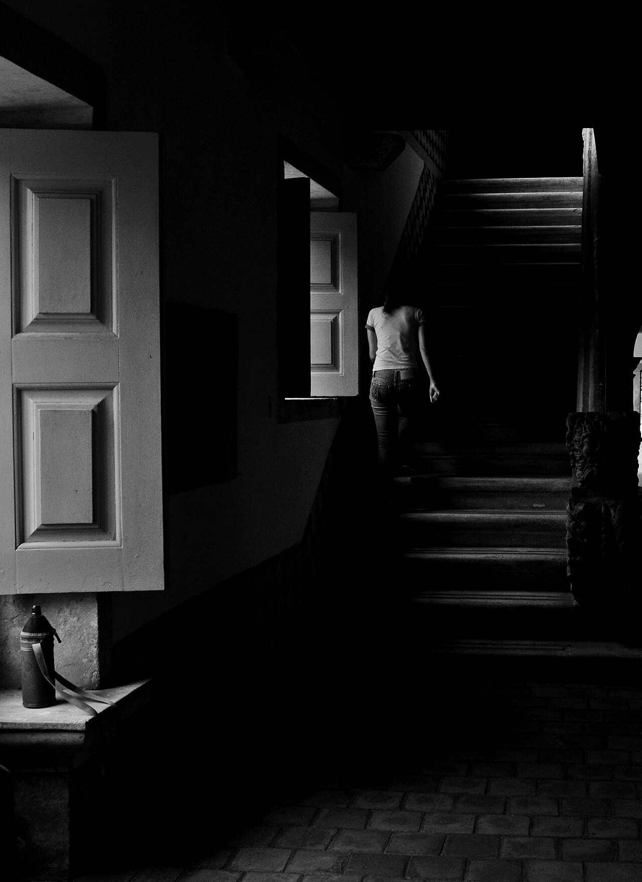 Interior do Centro Cultural São Francisco em preto e branco, com escadaria, uma pessoa de costas e janelas de madeira abertas à esquerda.