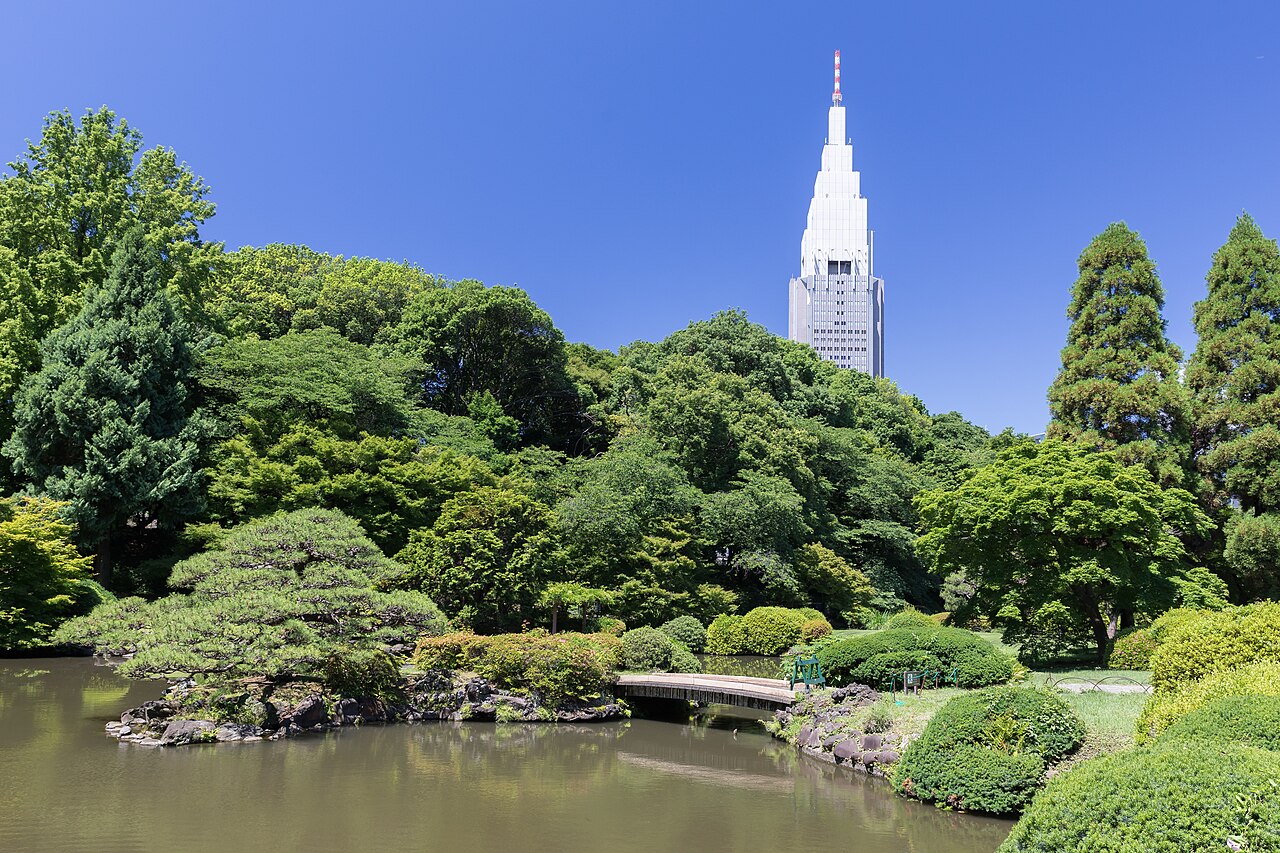 Ponte sobre lago no Shinjuku Gyoen, com edifício ao fundo.