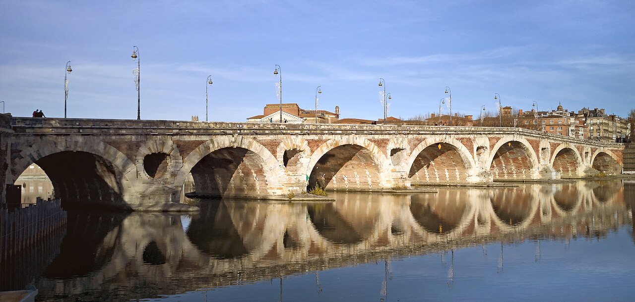 Arcos do Pont Neuf e edifícios ao fundo refletidos na água da Garonne sob céu azul.
