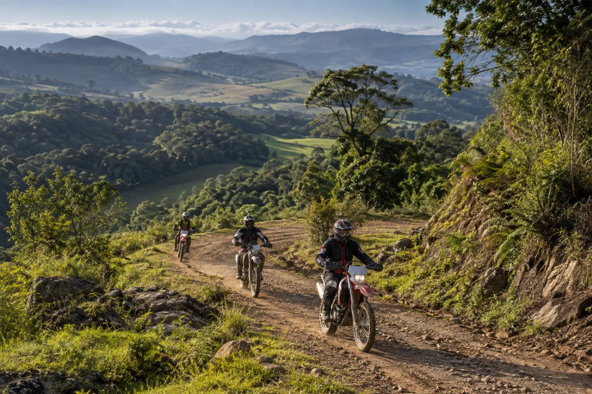 Ilustração por IA: Ilustração fotorrealista em formato horizontal 3:2 com três motociclistas usando equipamentos de proteção em um caminho de terra, entre vegetação e morros verdes sob luz natural. A cena é inspirada na região de Sapiranga, sem representar um local exato ou um registro da edição do evento.